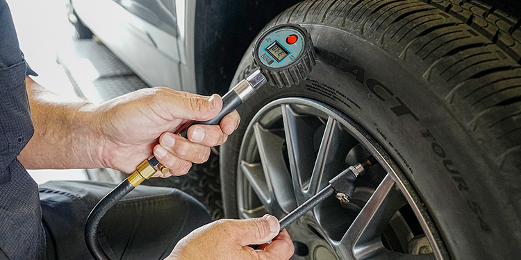 Technician checking car tire pressure with a digital tire pressure gauge during vehicle maintenance in an auto service garage.